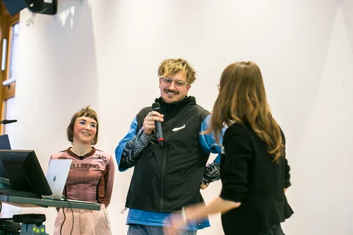 The artists Lex Rütten and Jana Kerima Stolzer are standing at a lectern, laughing and speaking with a third person.