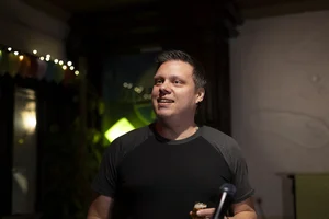 Hendrik zur Mühlen, with short hair and a black T-shirt, stands in front of a microphone and smiles warmly.