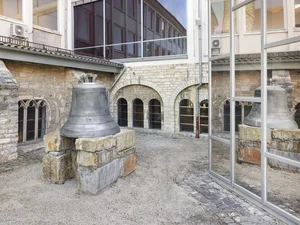 Das Bild zeigt den Innenhof des Stadtmuseums mit einer großen, alten Kirchenglocke auf einem steinernen Sockel, die sich in den Fenstern des Stadtmuseums spiegelt.