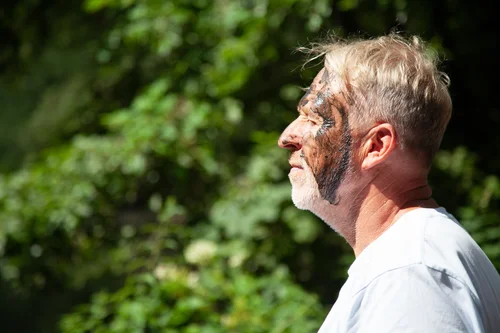 Ein Mann im Profil mit schlammverschmierten Gesicht. Er scheint das Sonnenlicht zu genießen.