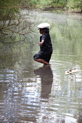 Der Performer steht im Wasser. Er hat ein Handtuch auf dem Kopf.