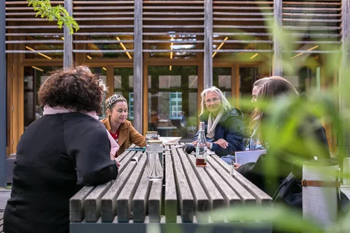 Four women are sitting around a wooden table outdoors, deeply engaged in conversation.