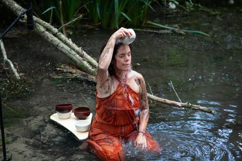 Die Künstlerin Daniela Brasil kniet in der Pader, und übergießt sich mit Wasser.
