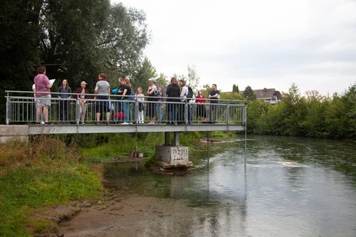 Eine Gruppe steht auf einem Steg, im Wasser ein Banner von Sophie Utikals Installation "I want to lay down with you".