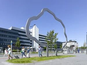 A tall metal sculpture, which forms the outline of a large tree, stands on a grass verge and surrounds a smaller tree. People walk past.
