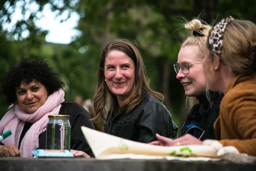 Four women are sitting at a table outdoors. They are discussing and laughing.